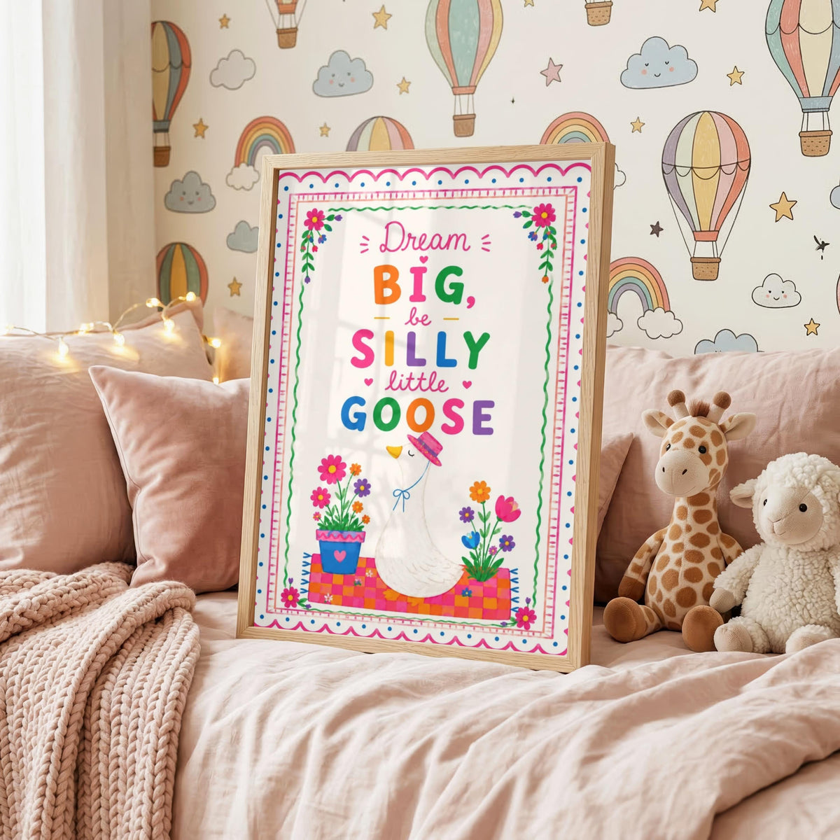 Framed goose wall art print resting on a pink bed with stuffed animals against a hot air balloon wallpaper.
