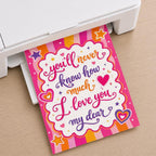 A colorful print with the text You'll never know how much I love you my dear coming out of a white home printer on a wooden surface.