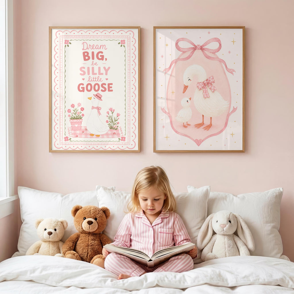 A young girl in pink pajamas sits on a white bed reading a book, with two framed pink nursery art prints hanging on the pink wall above her.