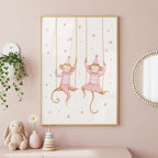 A framed watercolor print in a pink room shows two monkeys wearing striped shirts and party hats on swings, surrounded by stars.