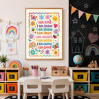 Framed affirmation print centered on a wall above a child's desk and two white chairs, with a chalkboard to the right.
