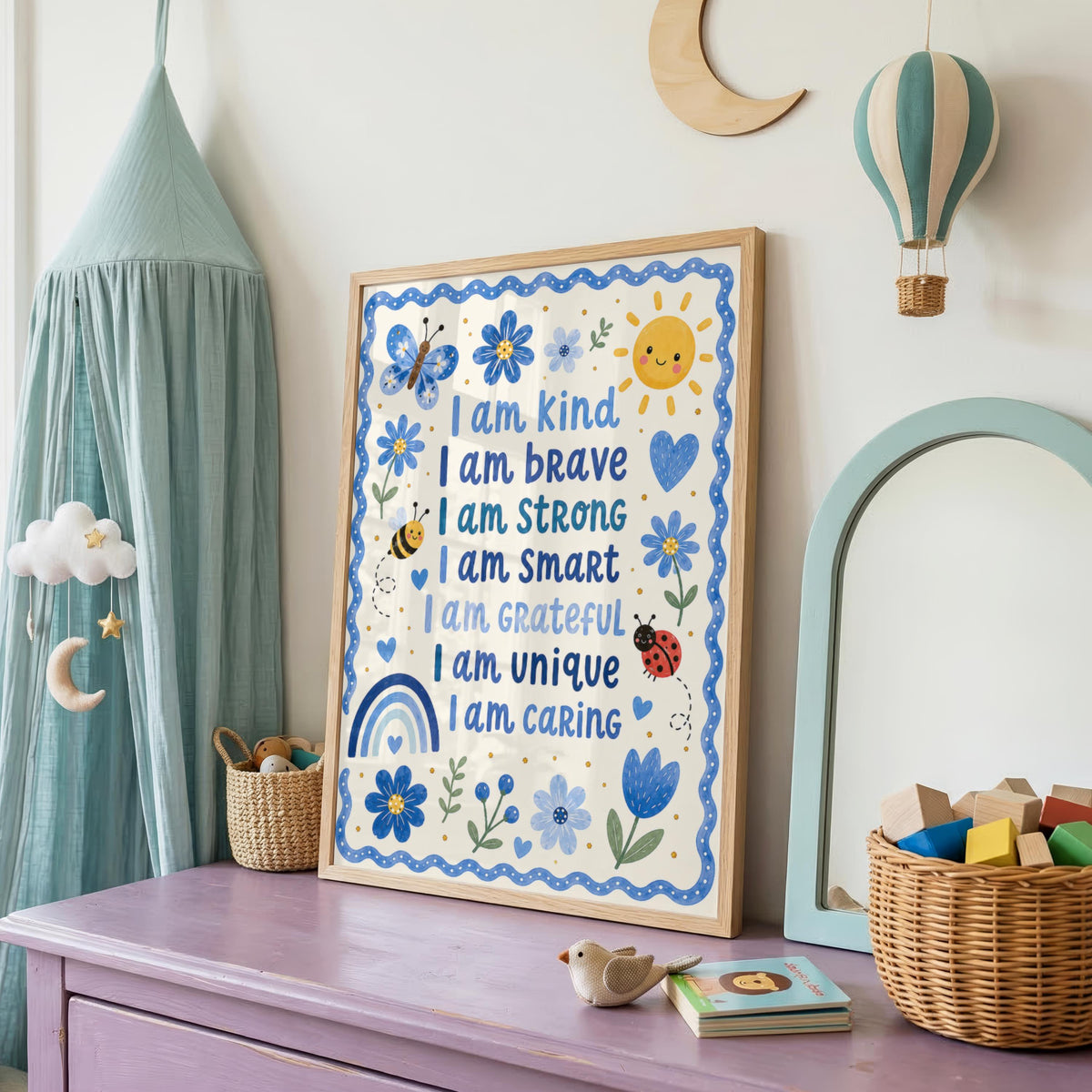 A framed children's affirmation print hangs on a white wall in a nursery next to a canopy bed, with a toy hot air balloon and a mirror.
