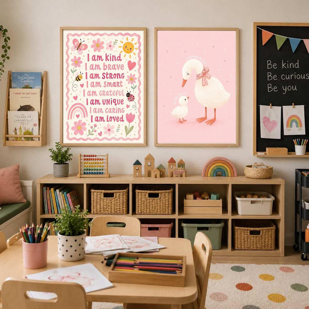 Two framed posters on a white wall, featuring a pink duck family art print next to an affirmation print, above a low wooden storage cubby.