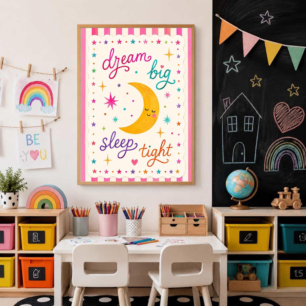 A framed wall art print showing a smiling moon graphic and dream big sleep tight text is displayed above a children craft table and a chalkboard wall with chalk drawings.