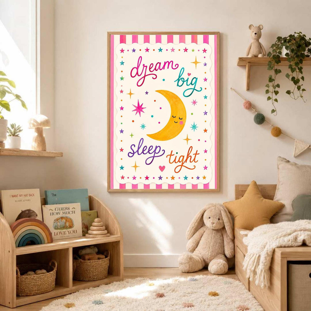 A framed nursery art print featuring a smiling moon and the quote dream big sleep tight hangs on a white wall above a low wooden toy shelf in a brightly decorated bedroom.