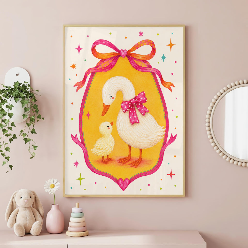 A whimsical framed print showing a mother goose with a pink bow and her duckling inside a pink frame, displayed on a pink wall next to a wall hanging plant and a round mirror.