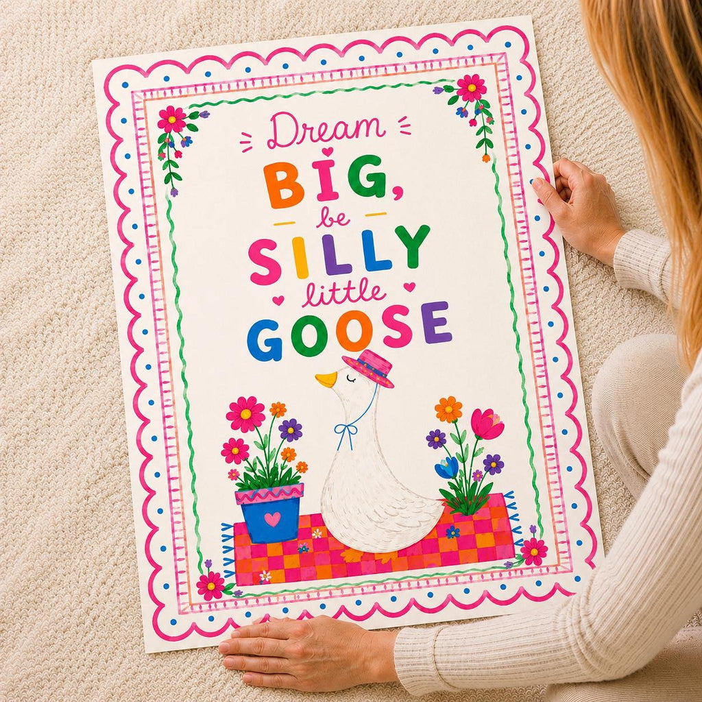 Person holding a colourful illustrated goose poster with floral borders and text reading Dream BIG be SILLY little GOOSE.