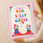 Person holding a colourful illustrated goose poster with floral borders and text reading Dream BIG be SILLY little GOOSE.