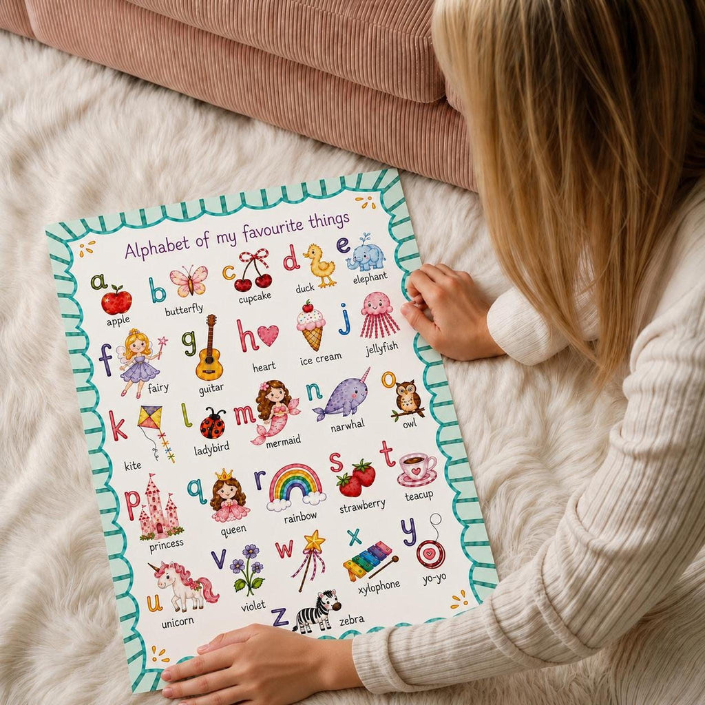 A person in a cream sweater sits on a white shag rug and holds the bottom edges of an illustrated alphabet poster.