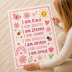 A person holds a large children's affirmation poster with pink text and floral illustrations against a textured white carpet.