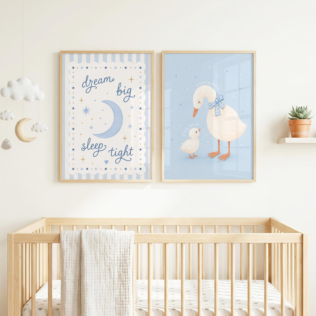 Two framed blue nursery art prints hang above a wooden crib, featuring a moon and stars on the left and two ducks on the right.