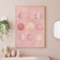 A framed pink solar system art print hangs on a pink wall above a shelf holding toys and a potted plant.