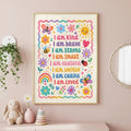 A framed children's affirmation poster hangs on a pink wall above a shelf with a stuffed bunny, a flower vase, and a stacking toy.
