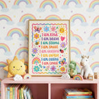The framed affirmation poster rests on a pink shelf in front of a rainbow-patterned wallpaper, flanked by plush toys.