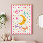 Framed nursery print with a smiling yellow moon, colorful stars, and the text dream big sleep tight, hanging on a pink wall above a stuffed bunny and stacking rings.