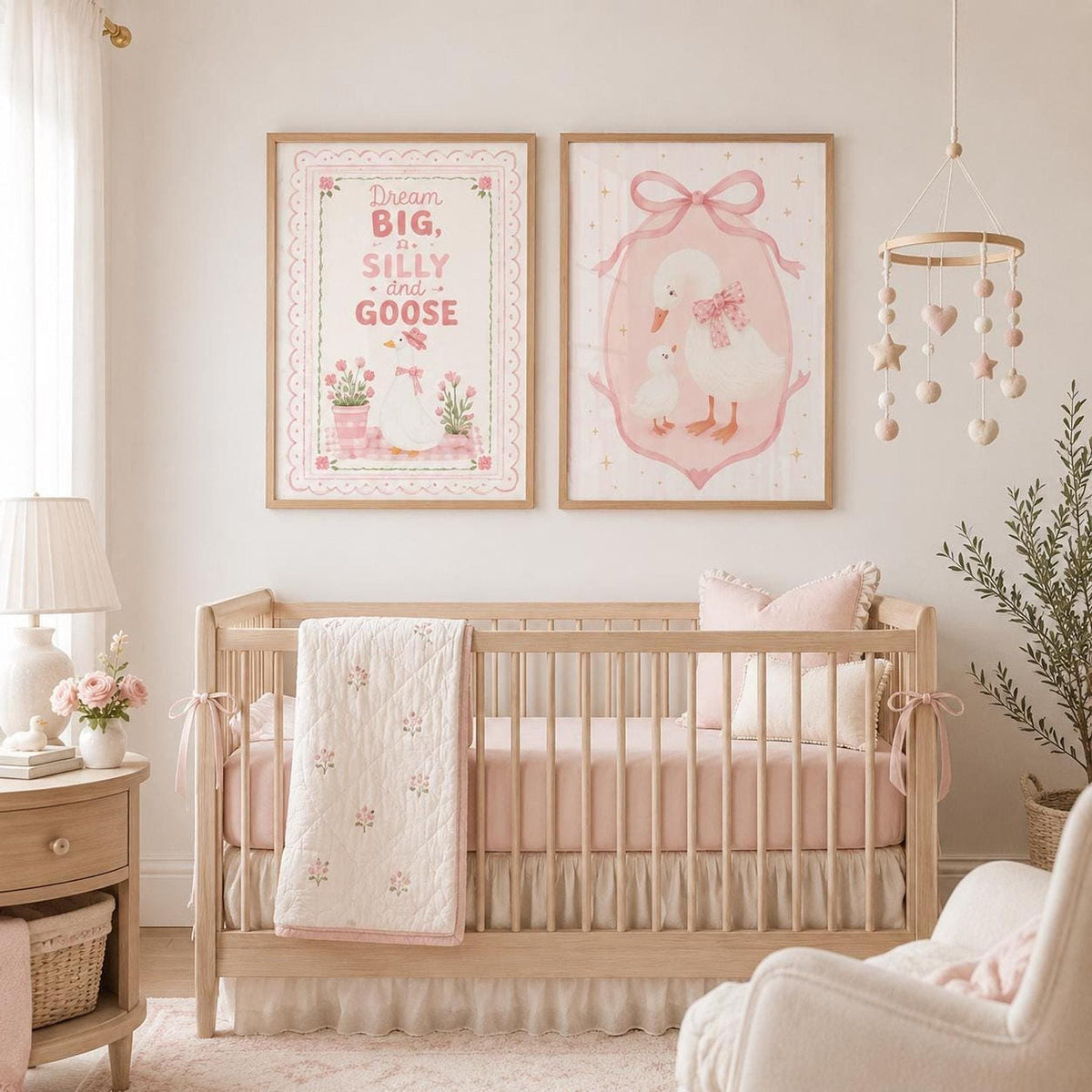 Set of two pink goose nursery wall prints displayed in light wood frames above a natural wooden cot, styled in a soft baby girl nursery with blush bedding, floral quilt, neutral furniture, hanging mobile and delicate pastel decor.