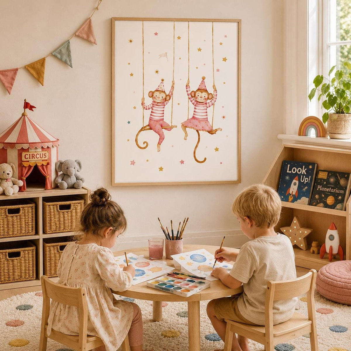 Pink circus monkey wall print displayed in a light wood frame above two children painting at a small table, styled in a bright playroom with circus tent decor, books, rocket toys, woven storage baskets, bunting and warm neutral furnishings.