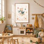 A framed watercolor print of a teddy bear reading a book on a cloud hangs above a children's play kitchen in a sunny room.