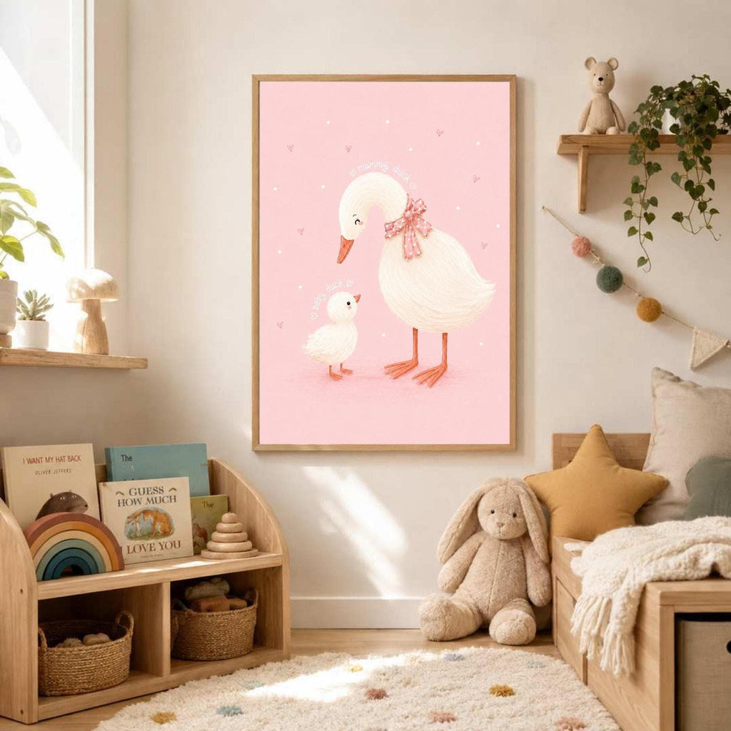 Framed pink duck family art hanging on a white wall above a wooden shelving unit filled with books and toys in a nursery.