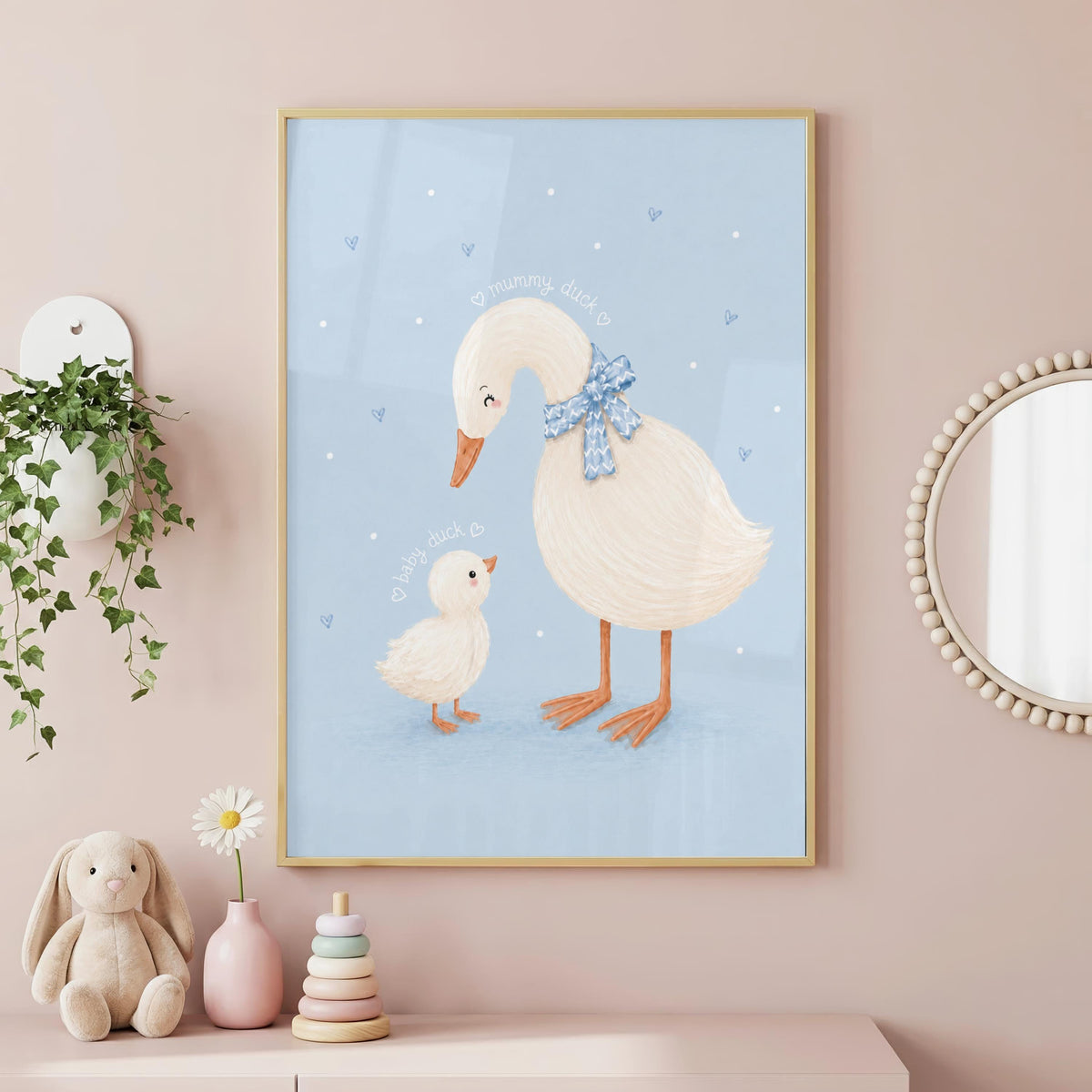 A framed illustration of a mother and baby duck on a light blue background hangs on a pink wall above a dresser with toys and a plant.