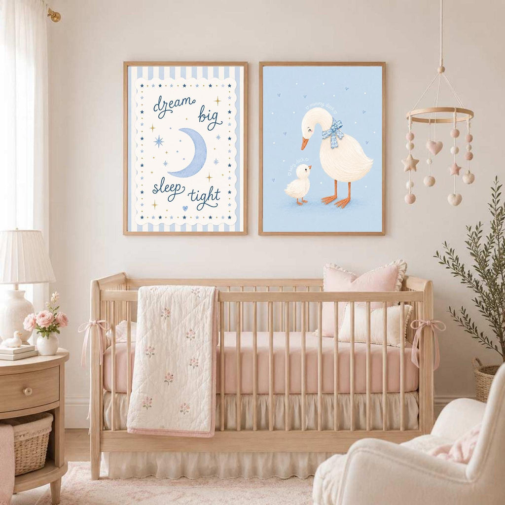 Two framed prints hang above a crib in a nursery, featuring a moon-and-stars graphic and a mother and baby duck illustration.