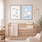Two framed prints hang above a crib in a nursery, featuring a moon-and-stars graphic and a mother and baby duck illustration.