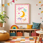 A framed nursery print with the text dream big sleep tight and a smiling moon hangs on a white wall above a low wooden shelf filled with toys in a colorful child bedroom.