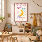 A child room features a framed print that reads dream big sleep tight with a crescent moon illustration centered on the white wall above a play kitchen and a wooden toy crate.
