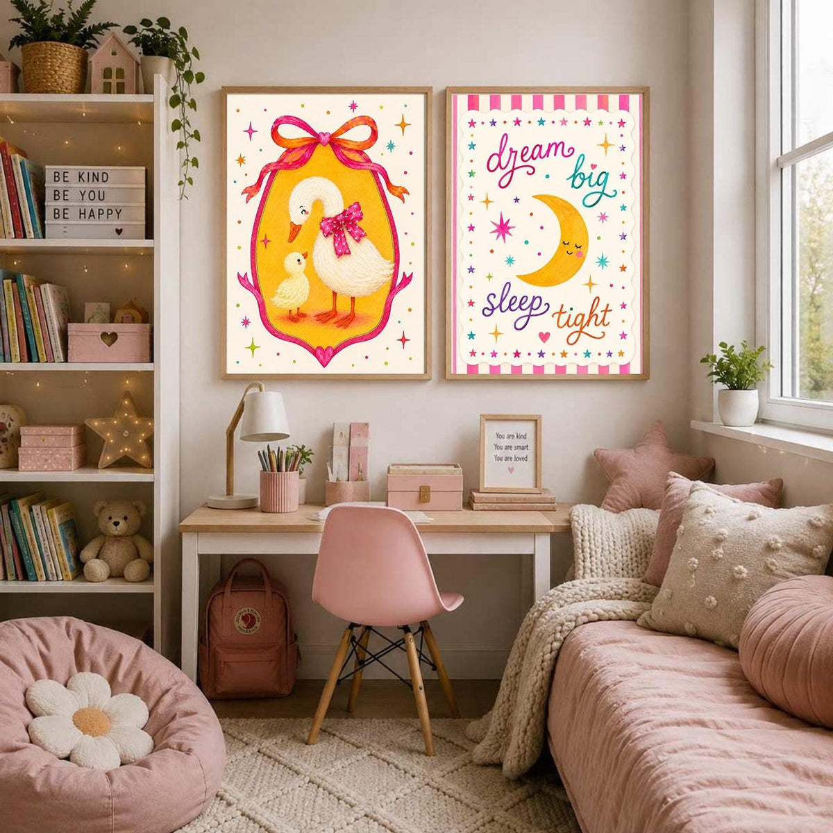 A framed print of a sun and flowers and a framed goose print hang on a pink wall above a baby's crib with pink bedding and a mobile.