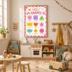 A framed basic shapes educational poster hangs on a wall above a childs play kitchen in a playroom.