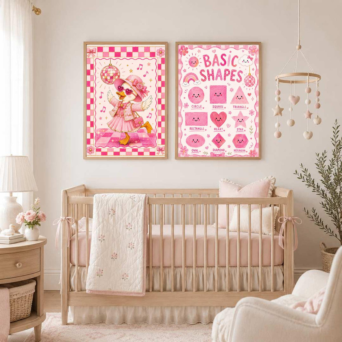 Two framed pink posters hang on a wall above a wooden crib in a nursery with pink bedding and decor.