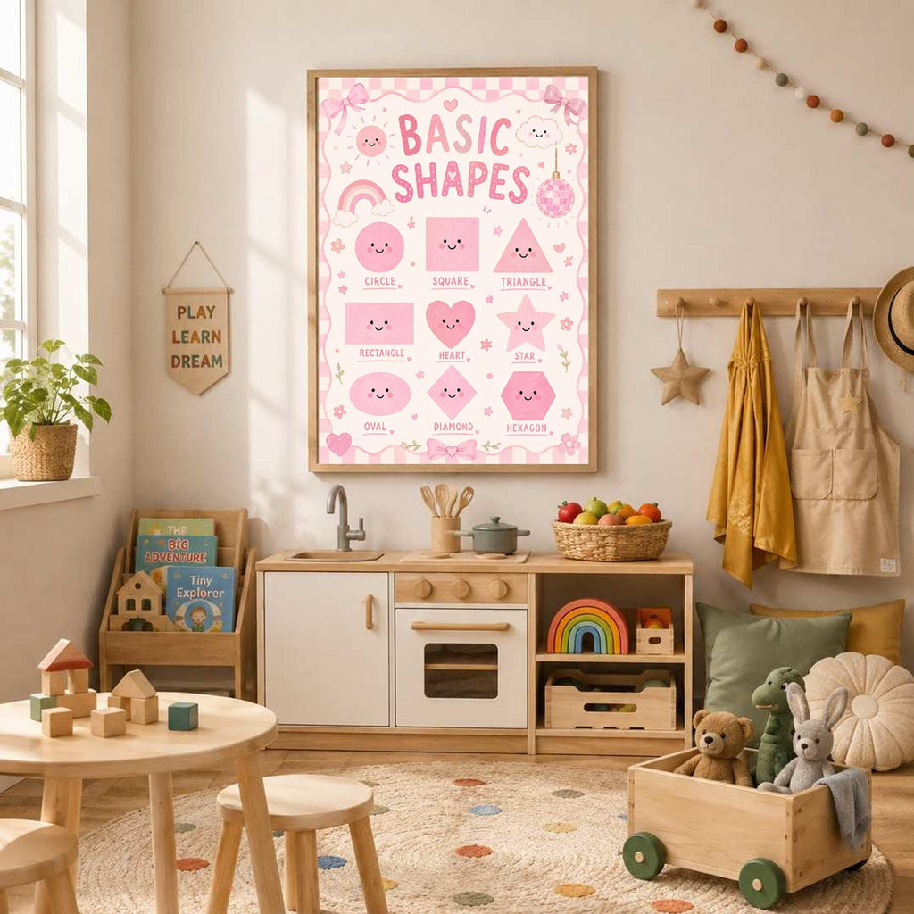 A framed pink educational poster reading Basic Shapes hangs in a childs playroom above a wooden play kitchen and table.