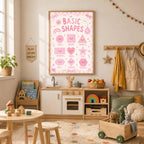 A framed pink educational poster reading Basic Shapes hangs in a childs playroom above a wooden play kitchen and table.