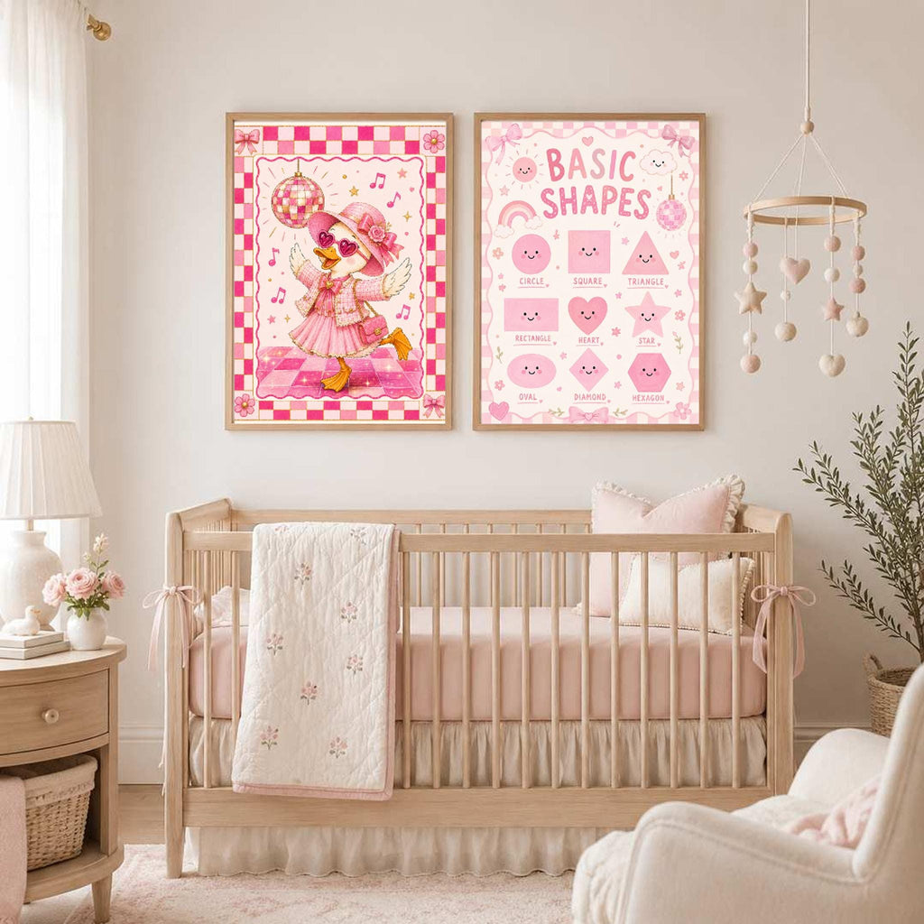 Two framed pink posters featuring a dancing duck and basic shapes hang on a wall above a wooden crib.