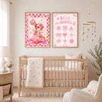 Two framed pink posters featuring a dancing duck and basic shapes hang on a wall above a wooden crib.
