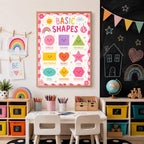 A framed basic shapes educational poster is mounted on a wall above a childs desk next to a blackboard.