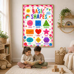 Two young children sit on a white rug reading a book below a framed basic shapes educational poster.