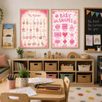 Two framed posters, one of an alphabet and one of basic shapes, hang on a wall above a long shelving unit in a study room.