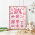 Pink educational shapes wall print featuring smiling circle, square, triangle, rectangle, heart, star, oval, diamond and hexagon shapes with a rainbow, flowers, clouds and playful pink details.